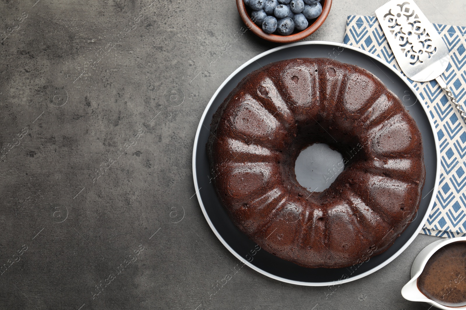Tasty chocolate bundt cake, blueberries and server on grey table, flat lay. Space for text Photo of Tasty chocolate bundt cake, blueberries and server on grey table, flat lay. Space for text