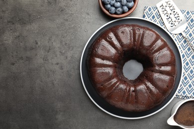 Photo of Tasty chocolate bundt cake, blueberries and server on grey table, flat lay. Space for text