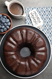 Photo of Tasty chocolate bundt cake, blueberries and server on grey table, flat lay