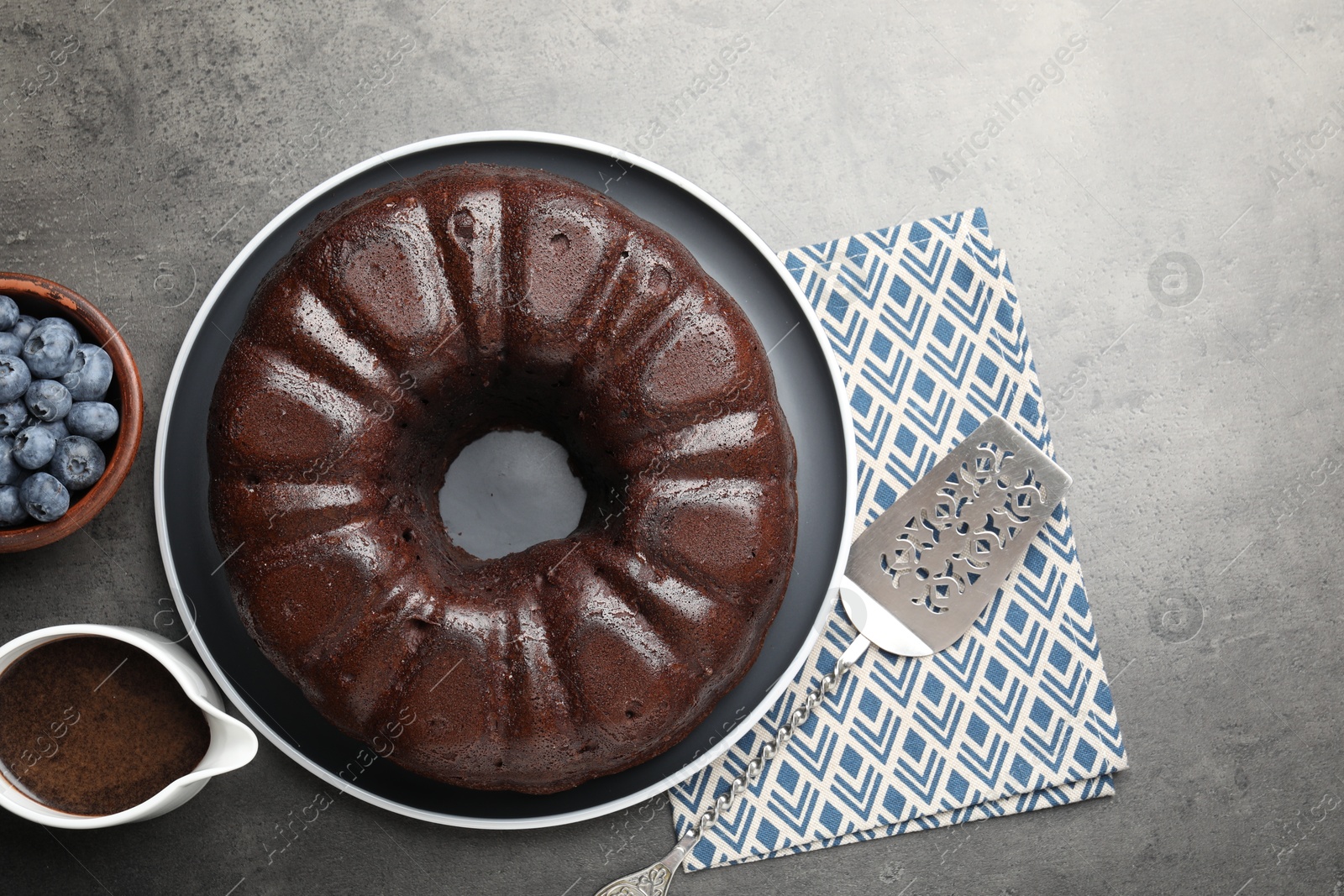 Tasty chocolate bundt cake, blueberries and server on grey table, flat lay Photo of Tasty chocolate bundt cake, blueberries and server on grey table, flat lay
