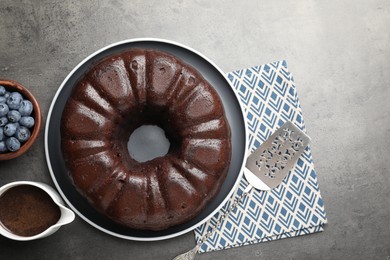 Photo of Tasty chocolate bundt cake, blueberries and server on grey table, flat lay