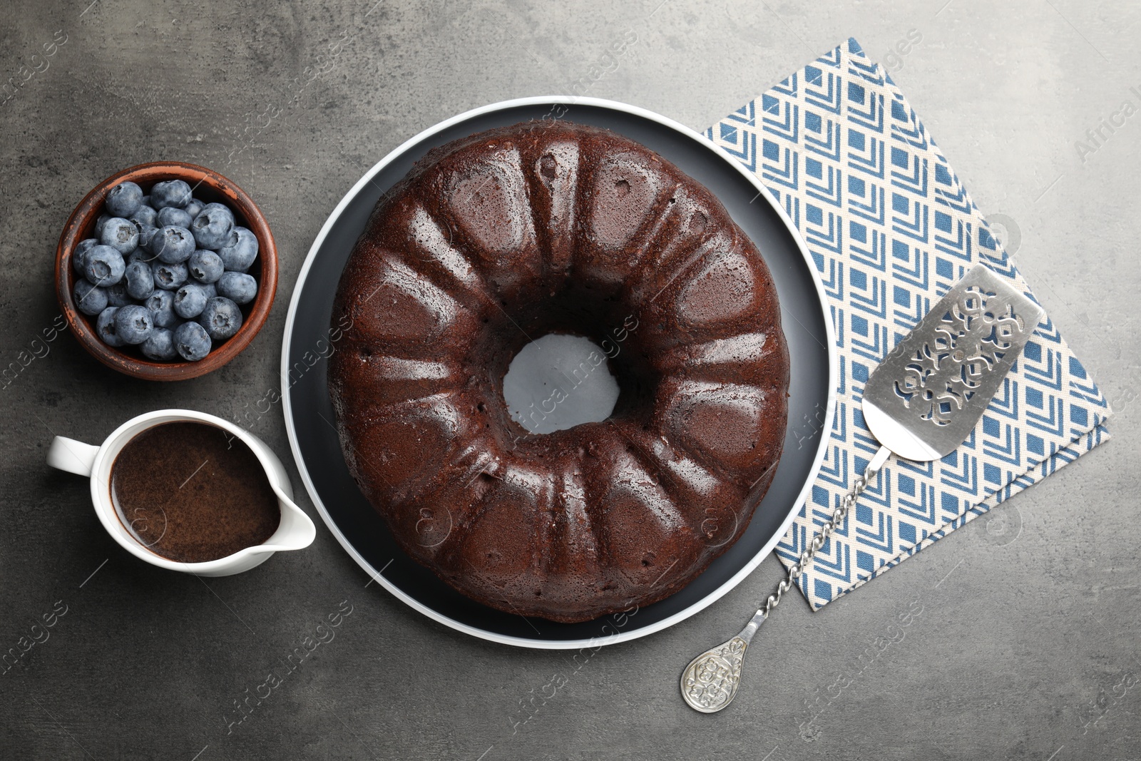 Tasty chocolate bundt cake, blueberries and server on grey table, flat lay Photo of Tasty chocolate bundt cake, blueberries and server on grey table, flat lay