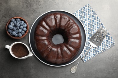 Photo of Tasty chocolate bundt cake, blueberries and server on grey table, flat lay