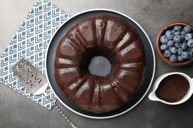 Photo of Tasty chocolate bundt cake, blueberries and server on grey table, flat lay