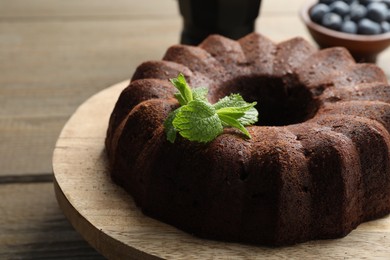 Photo of Tasty chocolate bundt cake with mint and blueberries on wooden table, closeup