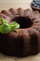 Photo of Tasty chocolate bundt cake with mint and blueberries on wooden table, closeup