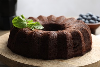 Photo of Tasty chocolate bundt cake with mint and blueberries on wooden table, closeup