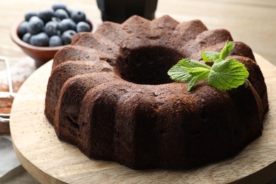 Photo of Tasty chocolate bundt cake with mint and blueberries on wooden table, closeup