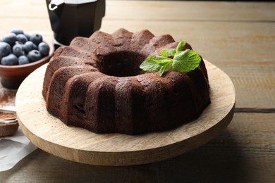 Photo of Tasty chocolate bundt cake with mint and blueberries on wooden table, closeup