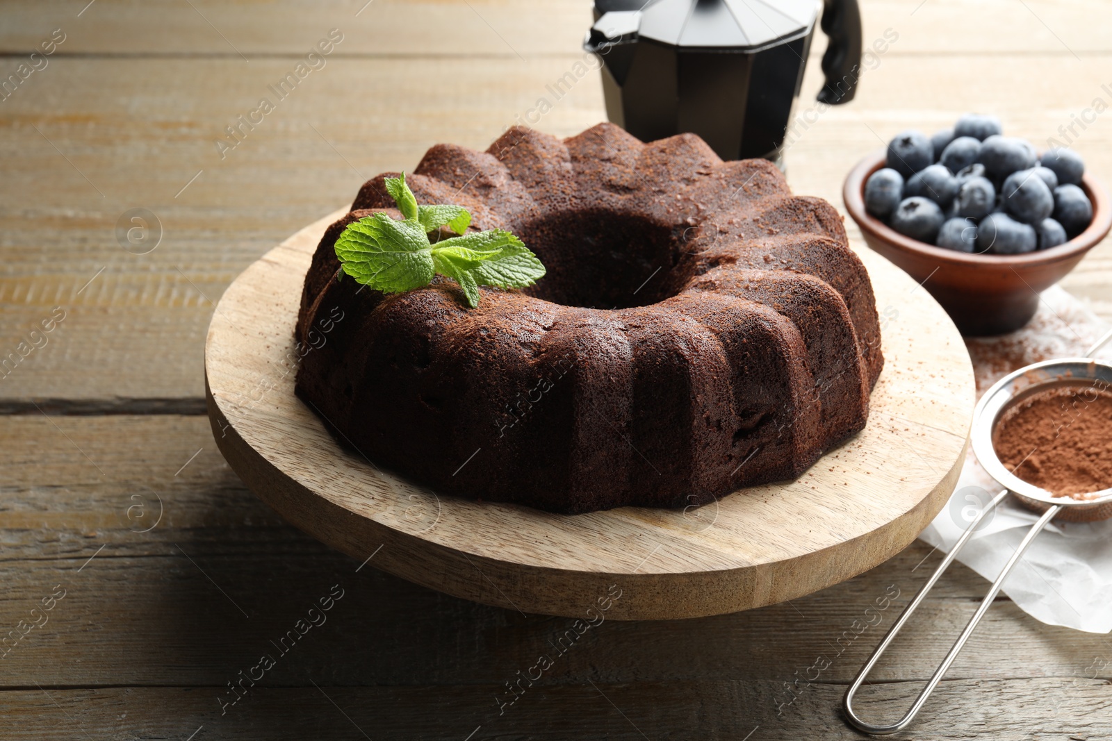 Tasty chocolate bundt cake with mint and blueberries on wooden table, closeup Photo of Tasty chocolate bundt cake with mint and blueberries on wooden table, closeup