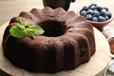 Photo of Tasty chocolate bundt cake with mint and blueberries on wooden table, closeup