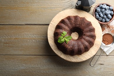Photo of Tasty chocolate bundt cake with mint and blueberries on wooden table, flat lay. Space for text