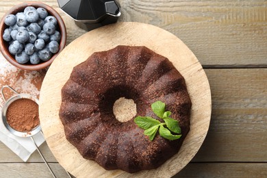 Photo of Tasty chocolate bundt cake with mint and blueberries on wooden table, flat lay