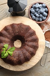 Photo of Tasty chocolate bundt cake with mint and blueberries on wooden table, flat lay