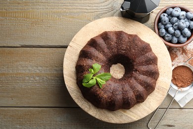 Photo of Tasty chocolate bundt cake with mint and blueberries on wooden table, flat lay. Space for text