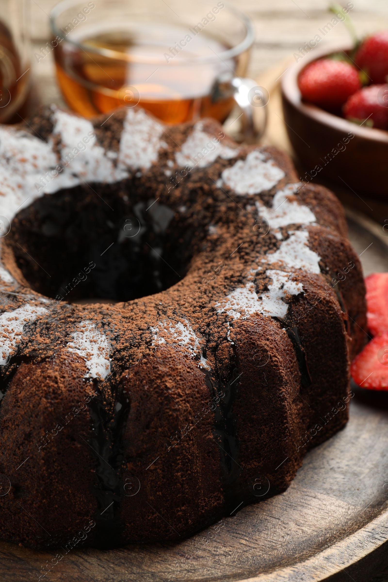 Tasty chocolate bundt cake with glaze, tea and berries on wooden table, closeup Photo of Tasty chocolate bundt cake with glaze, tea and berries on wooden table, closeup