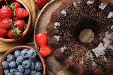 Photo of Tasty chocolate bundt cake with glaze and berries on wooden table, flat lay