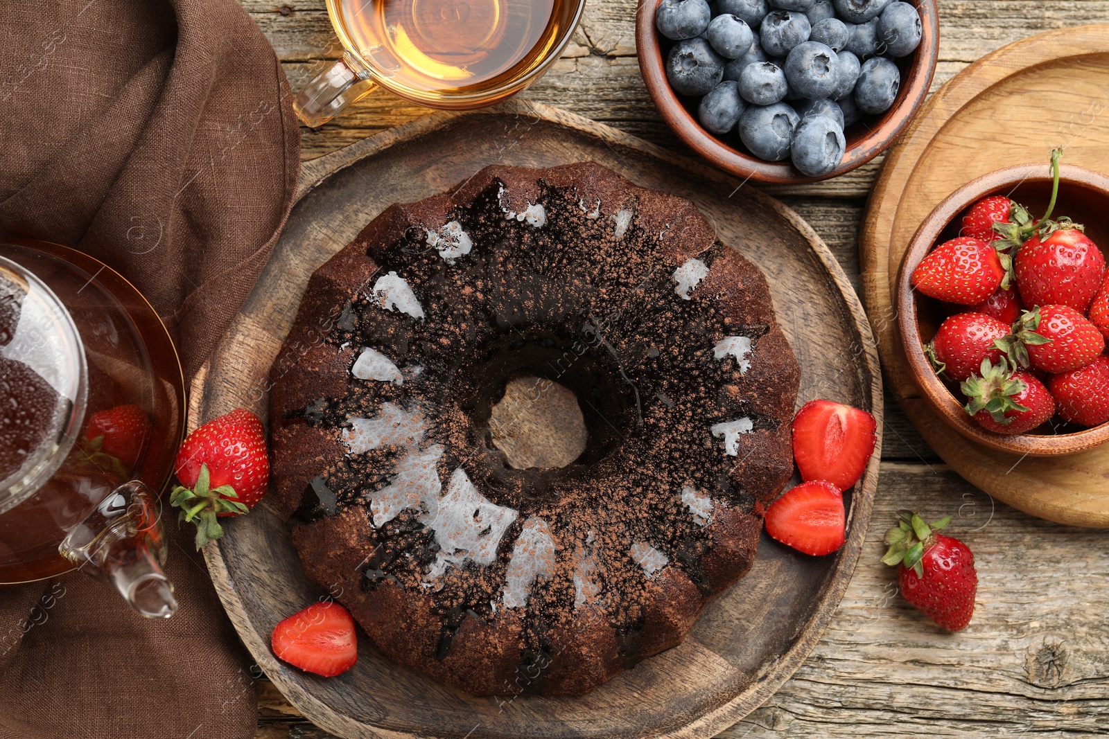 Tasty chocolate bundt cake with glaze, tea and berries on wooden table, flat lay Photo of Tasty chocolate bundt cake with glaze, tea and berries on wooden table, flat lay