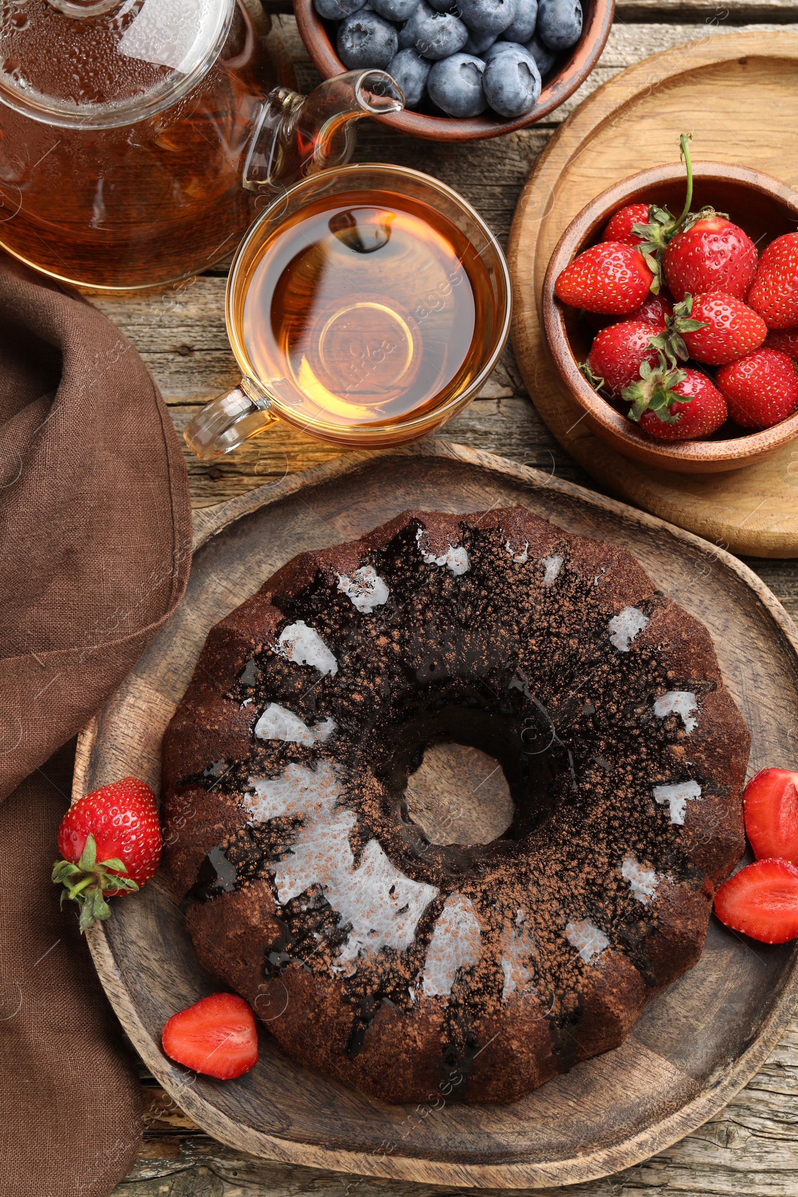Tasty chocolate bundt cake with glaze, tea and berries on wooden table, flat lay Photo of Tasty chocolate bundt cake with glaze, tea and berries on wooden table, flat lay