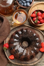 Photo of Tasty chocolate bundt cake with glaze, tea and berries on wooden table, flat lay