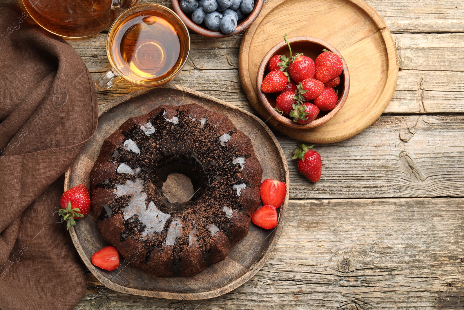 Tasty chocolate bundt cake with glaze, tea and berries on wooden table, flat lay Photo of Tasty chocolate bundt cake with glaze, tea and berries on wooden table, flat lay
