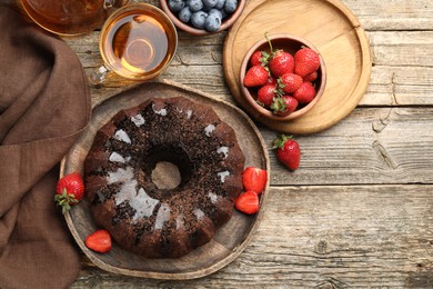 Photo of Tasty chocolate bundt cake with glaze, tea and berries on wooden table, flat lay