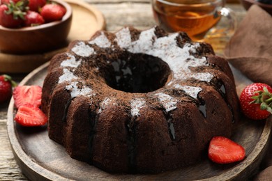 Photo of Tasty chocolate bundt cake with glaze, tea and berries on wooden table, closeup