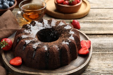 Photo of Tasty chocolate bundt cake with glaze, tea and berries on wooden table, closeup