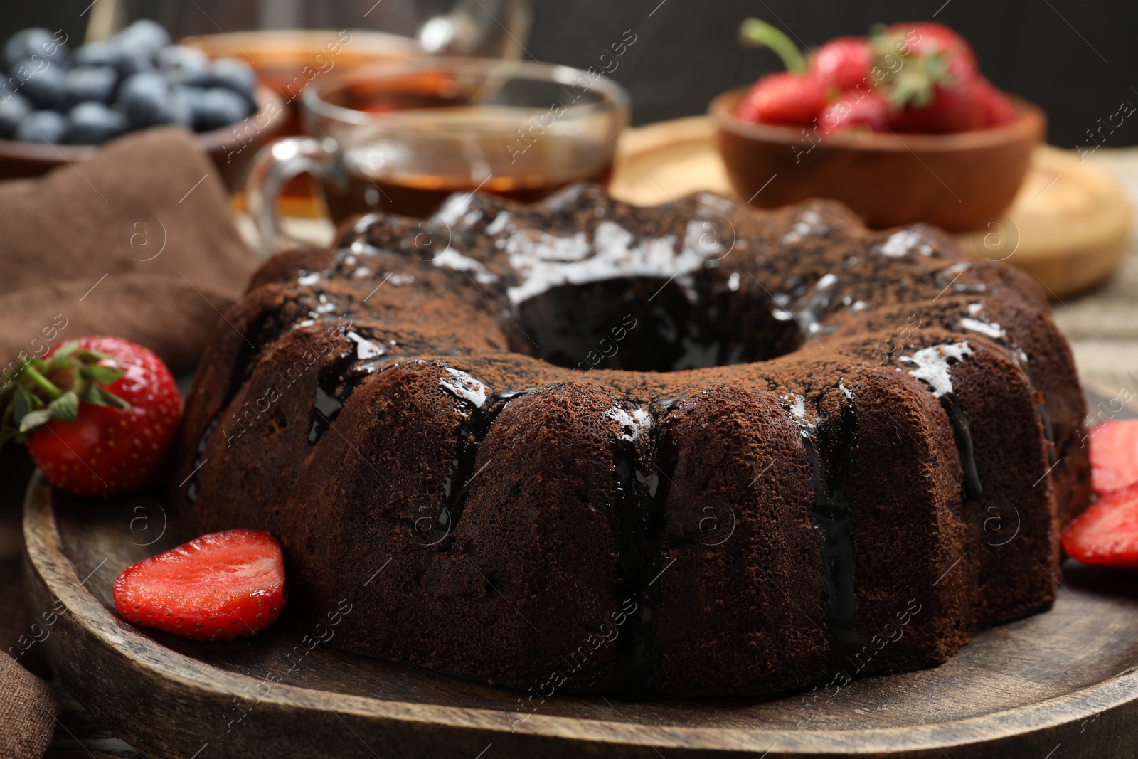 Tasty chocolate bundt cake with glaze, tea and berries on wooden table, closeup Photo of Tasty chocolate bundt cake with glaze, tea and berries on wooden table, closeup