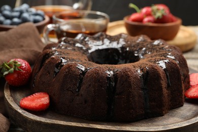 Photo of Tasty chocolate bundt cake with glaze, tea and berries on wooden table, closeup