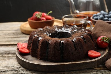 Photo of Tasty chocolate bundt cake with glaze, tea and berries on wooden table