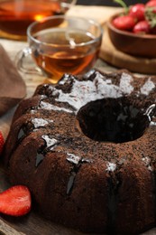 Photo of Tasty chocolate bundt cake with glaze, tea and berries on wooden table, closeup