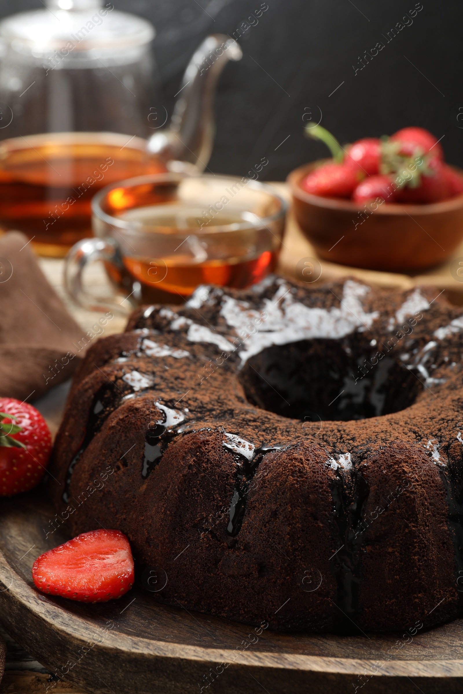 Tasty chocolate bundt cake with glaze, tea and berries on wooden table, closeup Photo of Tasty chocolate bundt cake with glaze, tea and berries on wooden table, closeup