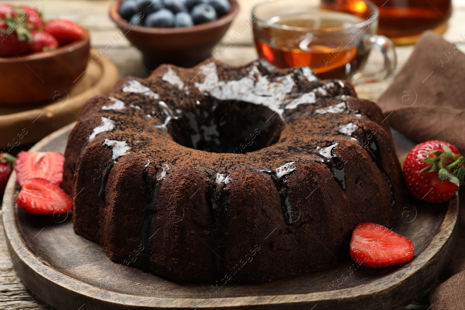 Tasty chocolate bundt cake with glaze, tea and berries on wooden table, closeup Photo of Tasty chocolate bundt cake with glaze, tea and berries on wooden table, closeup