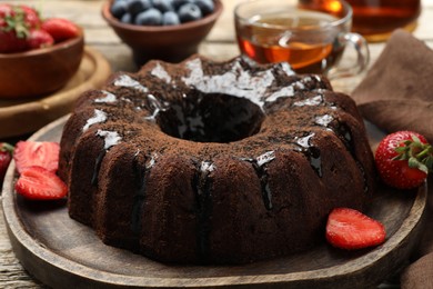 Photo of Tasty chocolate bundt cake with glaze, tea and berries on wooden table, closeup