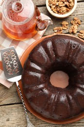 Photo of Tasty chocolate bundt cake, walnuts, tea and server on wooden table, flat lay