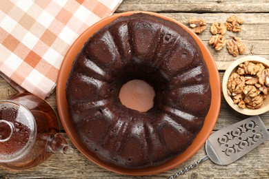 Photo of Tasty chocolate bundt cake, walnuts, tea and server on wooden table, flat lay
