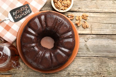Photo of Tasty chocolate bundt cake, walnuts, tea and server on wooden table, flat lay