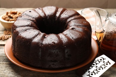 Photo of Tasty chocolate bundt cake, server, walnuts and tea on wooden table, closeup