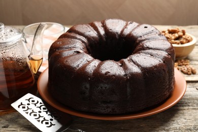 Photo of Tasty chocolate bundt cake, server, walnuts and tea on wooden table, closeup