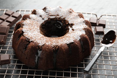 Photo of Tasty bundt cake with glaze and chocolate pieces on grey table, closeup