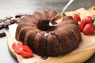Photo of Pouring glaze onto chocolate bundt cake at table, closeup