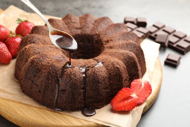 Photo of Pouring glaze onto chocolate bundt cake at table, closeup