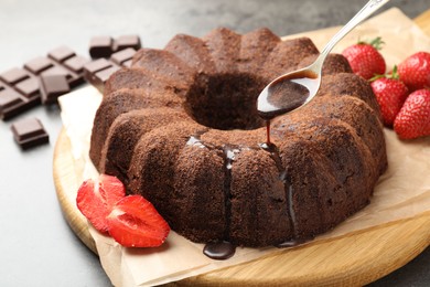 Photo of Pouring glaze onto chocolate bundt cake at table, closeup