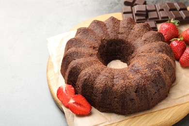 Photo of Tasty bundt cake, chocolate pieces and strawberries on grey table. Space for text