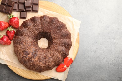 Photo of Tasty bundt cake, chocolate pieces and strawberries on grey table, flat lay. Space for text