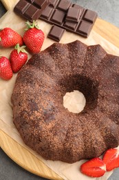 Photo of Tasty bundt cake, chocolate pieces and strawberries on grey table, flat lay