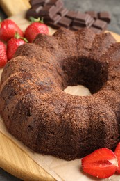 Photo of Tasty bundt cake, chocolate pieces and strawberries on grey table, closeup