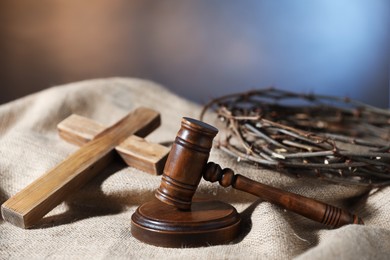 Photo of Judge's gavel, wooden cross and crown of thorns on burlap fabric, closeup