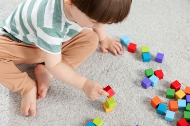 Photo of Cute little child playing with colorful cubes at home, above view
